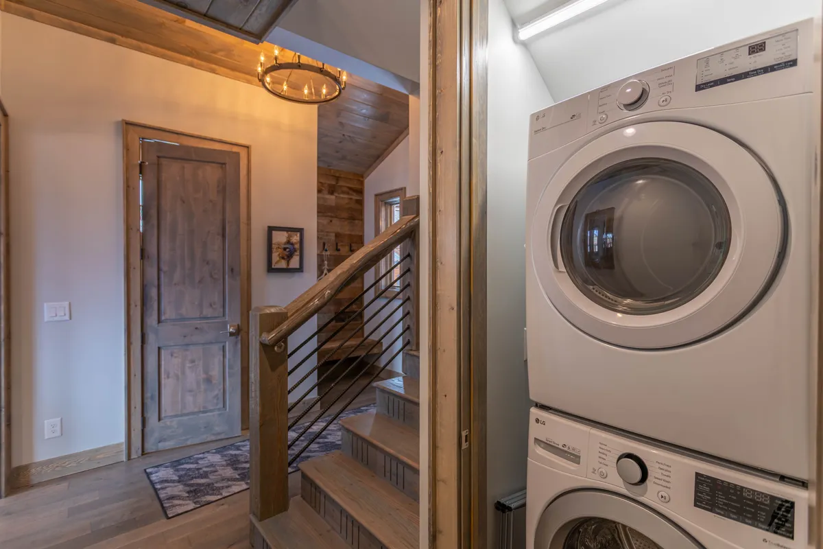 A bright utility area featuring a staircase, washer and dryer, entryway door, and a stylish chandelier. The space feels homey yet functional, with thoughtful design touches for efficient household management and convenience.
