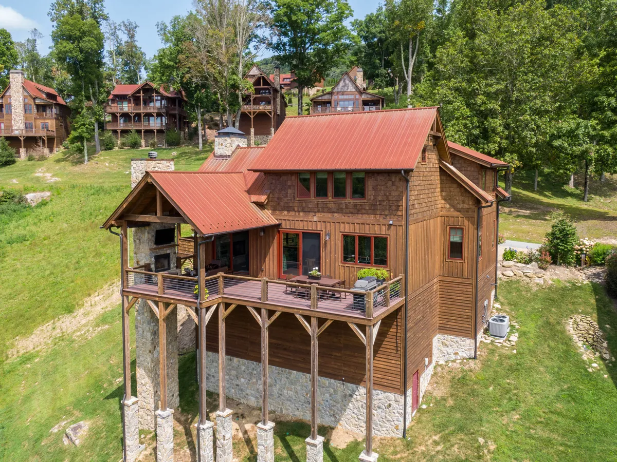 An inviting wooden deck with a red roof and sturdy stone pillars is surrounded by lush trees. The space is arranged for outdoor gatherings and relaxation, offering a direct visual connection to nature. The setting suggests ample opportunities for enjoying sunsets, watching wildlife, or unwinding after an active day outdoors.