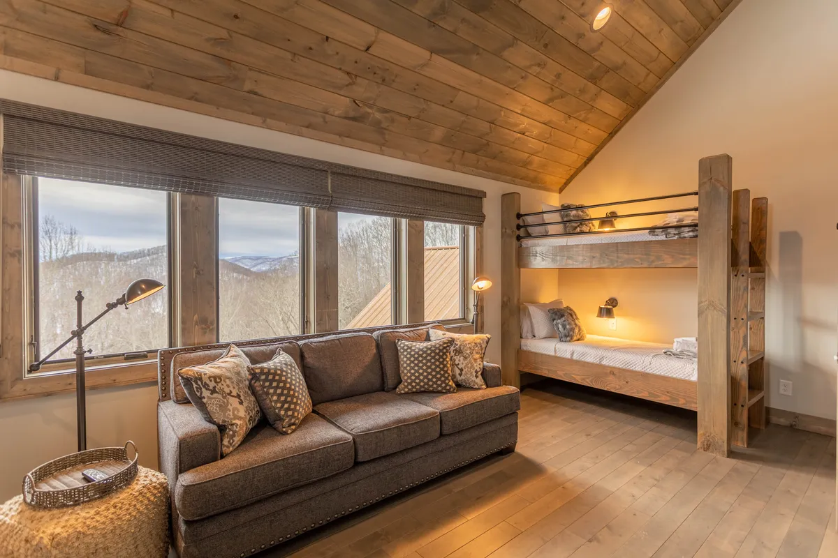 A cheerful bunk room with large windows offering mountain views, two sets of twin-over-twin bunk beds, and a cozy sofa for relaxation or group activities. The space feels welcoming and family-friendly.