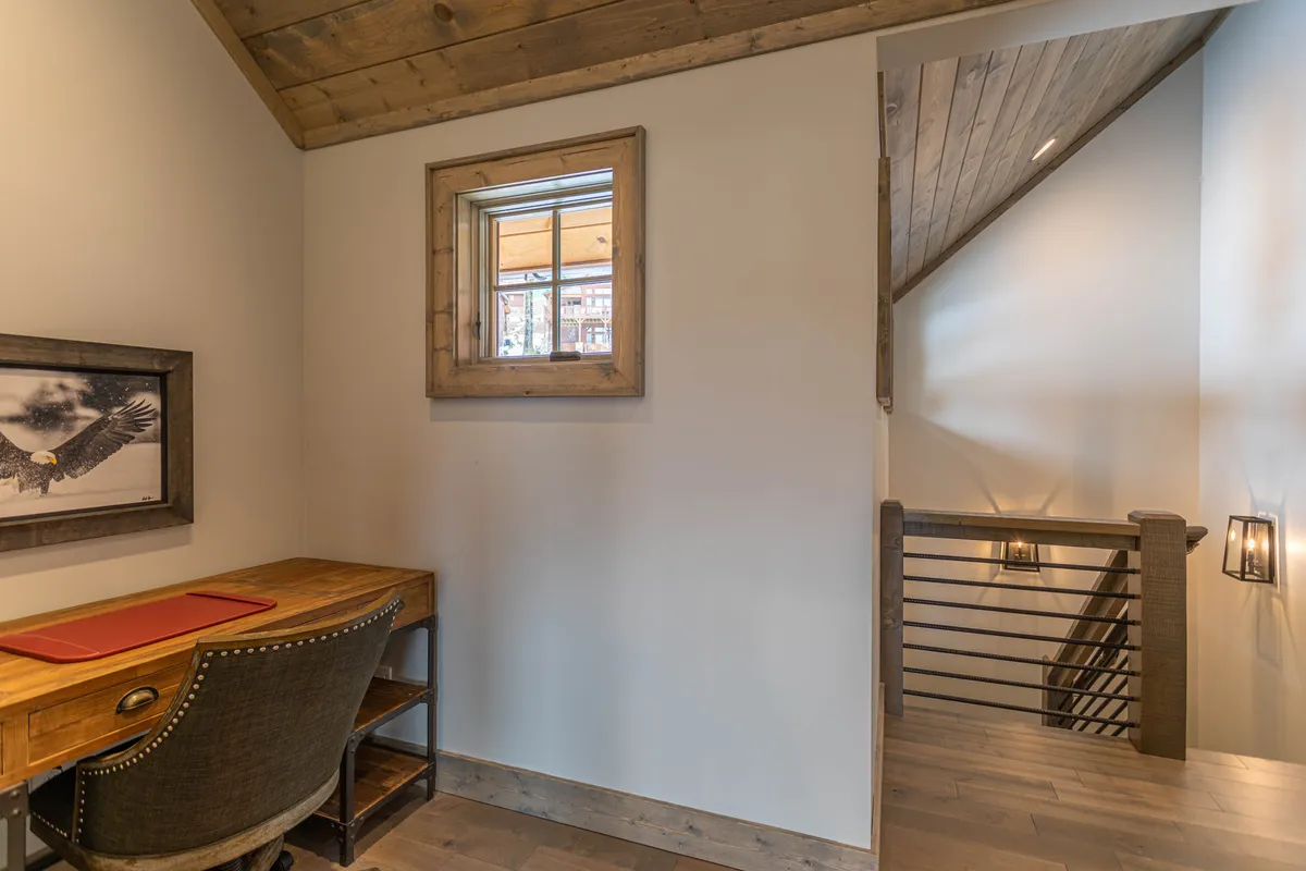 A compact, dedicated workspace tucked near a staircase, with a wooden desk, framed artwork, and ample natural light from a nearby window. The nook offers a productive but serene spot for work or creative pursuits.