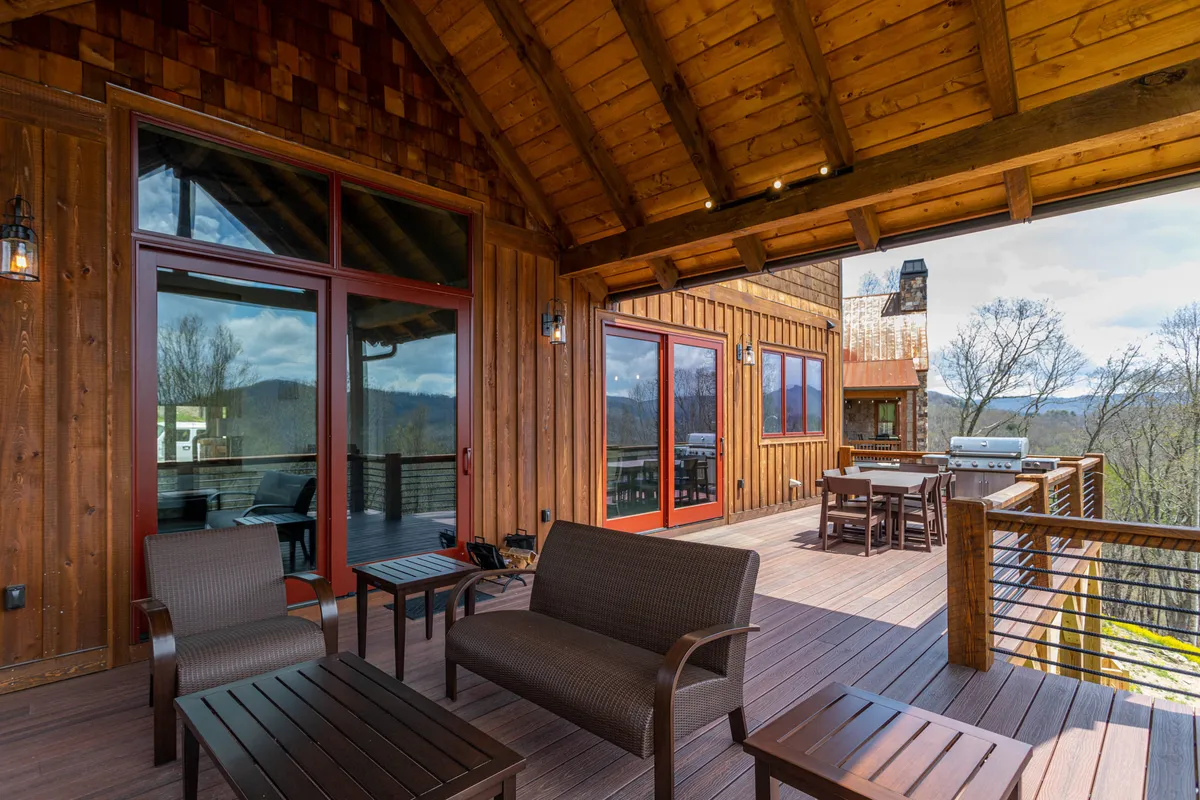 A spacious wooden deck with comfortable seating, an outdoor grill, dining table, and panoramic mountain views. The setting is perfectly arranged for al fresco meals, barbecuing, and relaxing moments with friends or family.